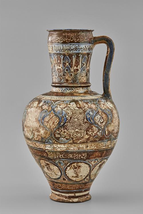 A ceramic jug with a slender handle, bulbous lower body, and rimmed opening. It is decorated with brown and blue against a white body, showing figures and floral medallions. There are five bands of inscriptions, with the handle painted in blue and brown.