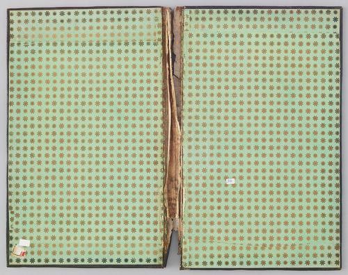 Interior of bookbinding covers, lime green, with gold repeated pattern of a eight petal flower and an image which loosely resembles a sun. The spine is visibly worn. 