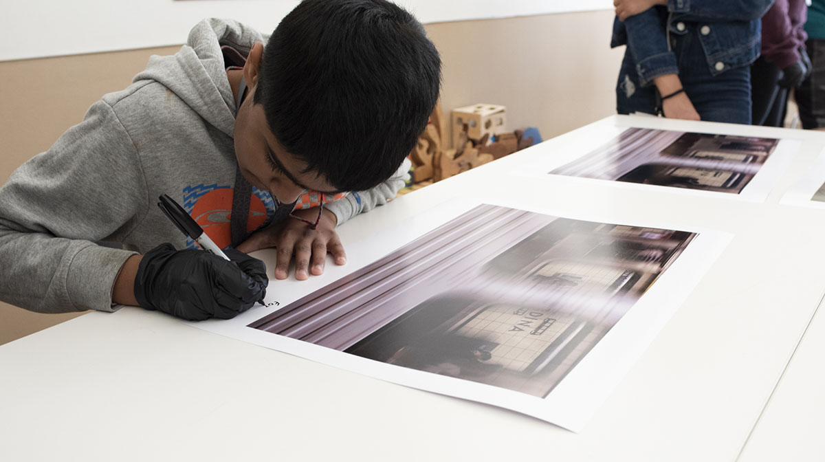 A student sitting at a desk writing his signature on a photograph.