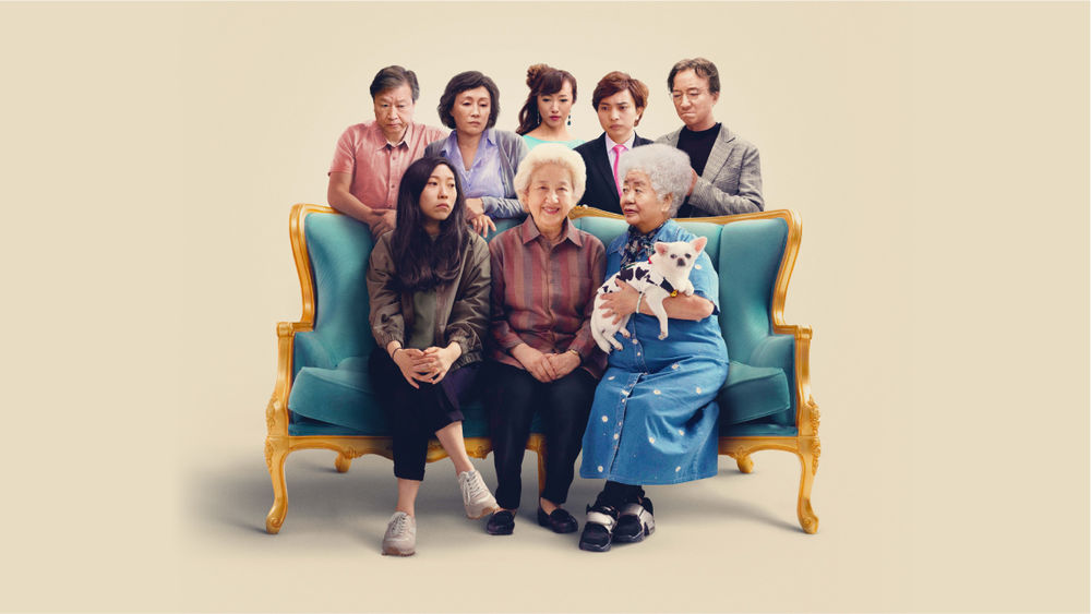 The grandmother sits on a blue couch surrounded by seven family members, one holding a white and black dog. 