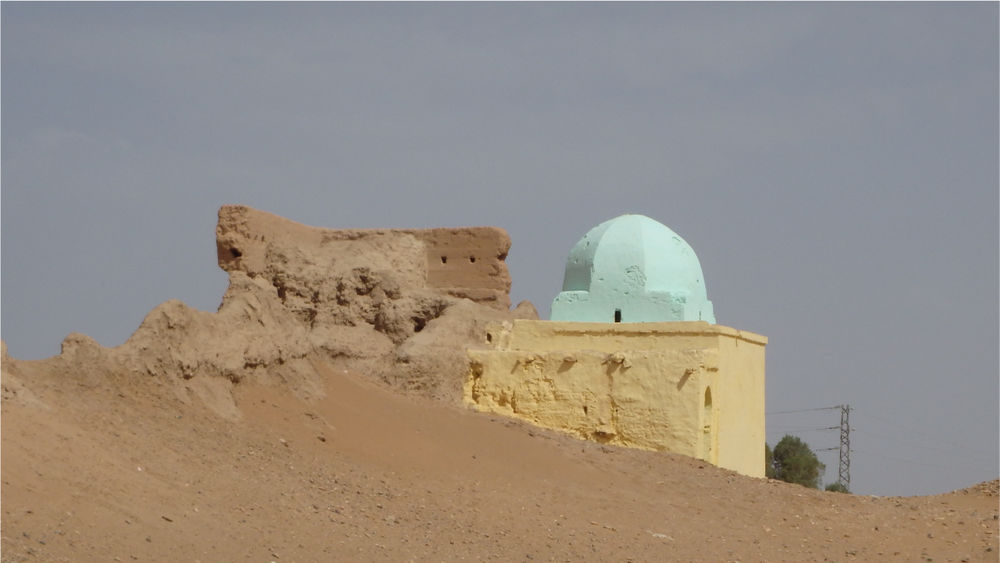 A pale green dome sits atop partly ruined walls emerging from sand dunes.