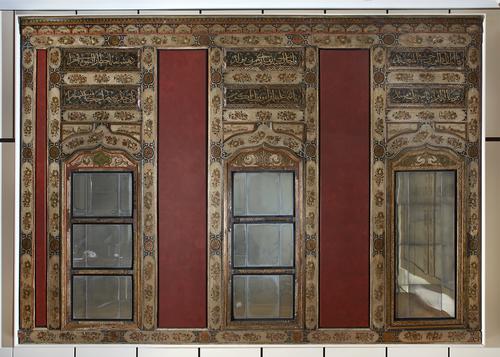 Three tall rectangular panels with cartouches filled with inscriptions and designs above rectangular mirror bottom of each. Each panel separated by a red rectangle 