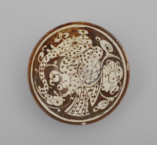 View of the inside of a circular bowl, decorated in a brown paint over a cream background. The bowl is painted with an elephant-headed bird surrounded by clouds, with bands of white and brown around the rim.