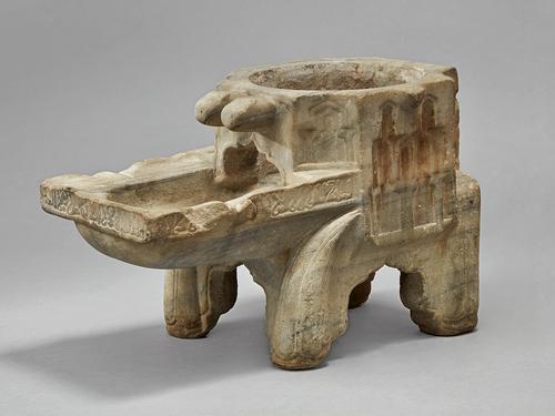 Irregular rectangular shaped object, with a hollow octagonal trunk featuring a circular opening on the top, extending from the front face of the object is a trough, resembling a pool that is supported by four legs carved of elaborately decorated marble.
