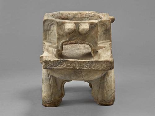 Front view of the irregular rectangular shaped object, with a hollow octagonal trunk featuring a circular opening on the top, extending from the front face of the object is a trough, resembling a pool that is supported by four legs carved of elaborately decorated marble.