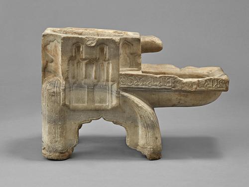 Side view of the irregular rectangular shaped object, with a hollow octagonal trunk featuring a circular opening on the top, extending from the front face of the object is a trough, resembling a pool that is supported by four legs carved of elaborately decorated marble.