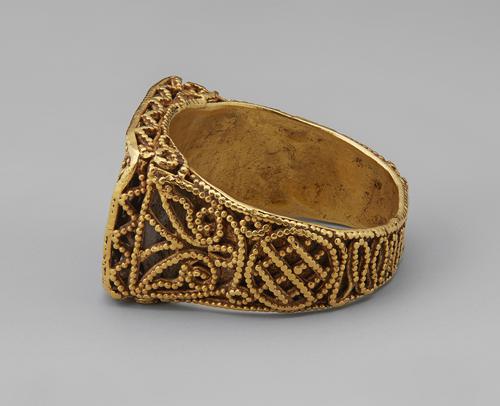 Side view of the Golden rectangular ring laying on its side. View of the granulated and filigree decoration on the side of the band.