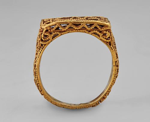 Golden rectangular ring standing straight up on its band. Side view of the filigree and granulation that create this ring.  