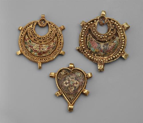 Three pendants, two closed crescent shaped and one heart shaped. All three are gold filigree and embellished with granulation, inlaid in the centre of each is an multicolour enamel plaque.