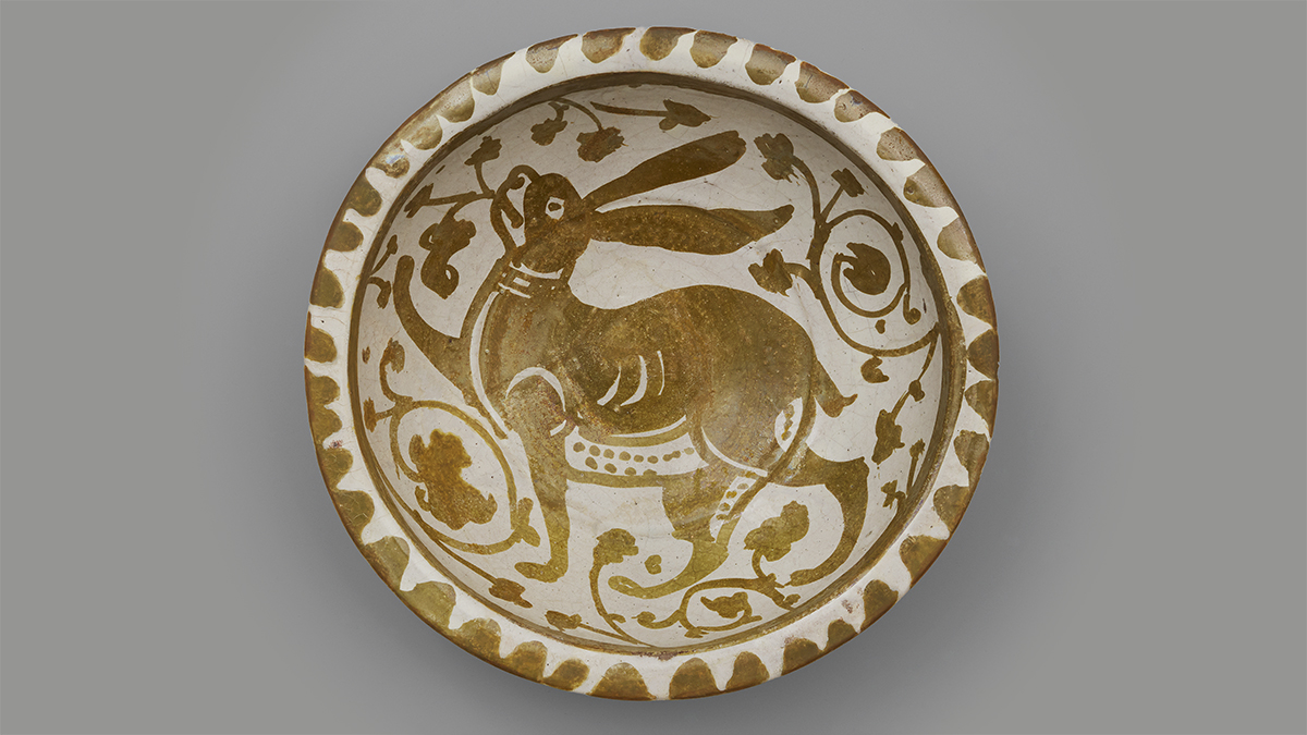 A ceramic bowl with a golden lustrous sheen, and a jovial long-eared hare painted at the centre.