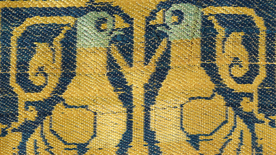 Two golden yellow embroidered birds face each other against a blue silk background. 