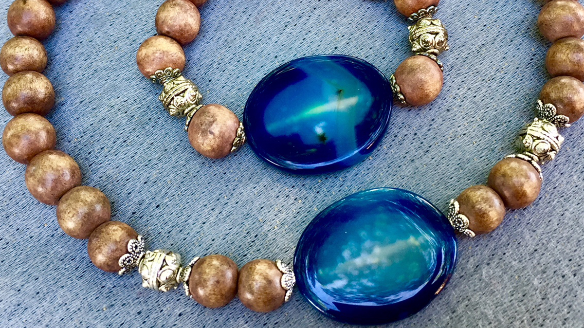 A beaded wooden bracelet with silver brackets and a large blue gem rests inside a matching necklace.