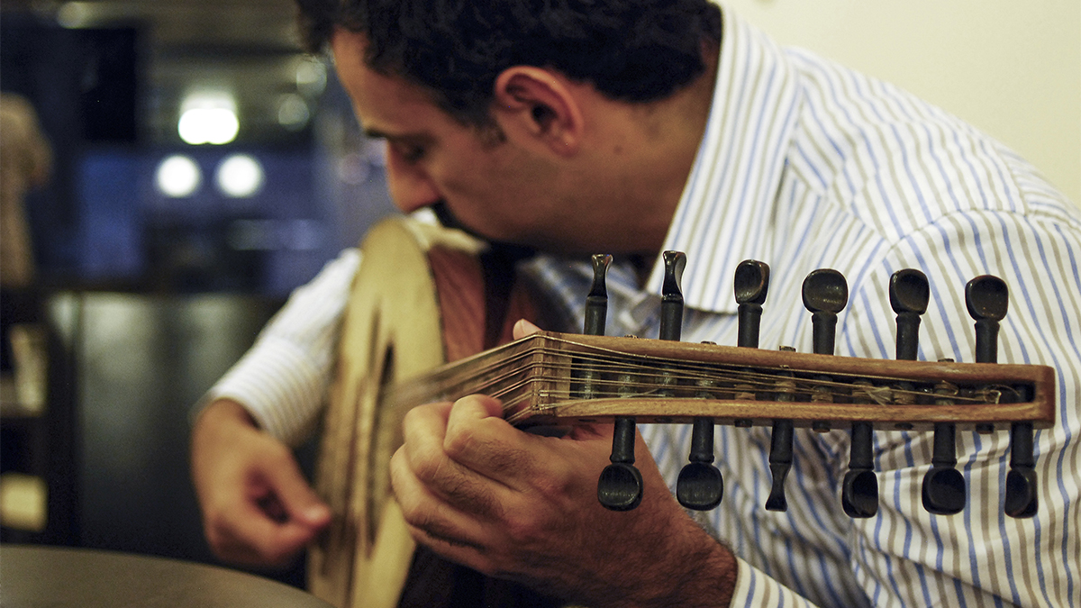 A man wearing a collared shirt plays the oud.