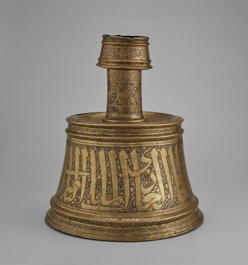 Candlestick with a conical base was hammered from brass sheet in two parts and soldered together, featuring large Arabic inscription on the base, and roundels on the neck.