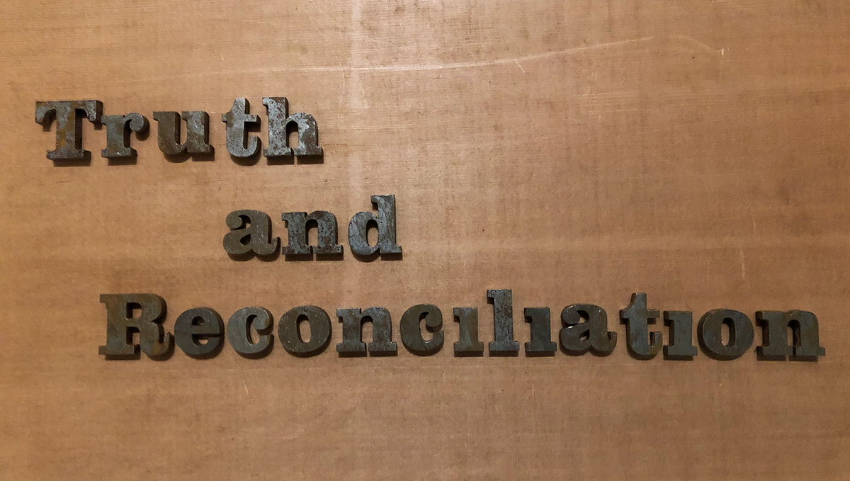 Rusting letters, laid out on a wooden surface, spelling out the phrase 'Truth and Reconcialition'