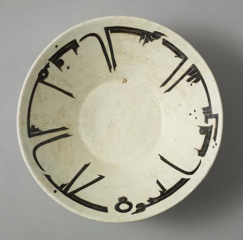 Bowl, with everted sides, decorated with a fine band of angular kufic inscription around the inner border, painted in manganese-brown against an opaque-white ground.