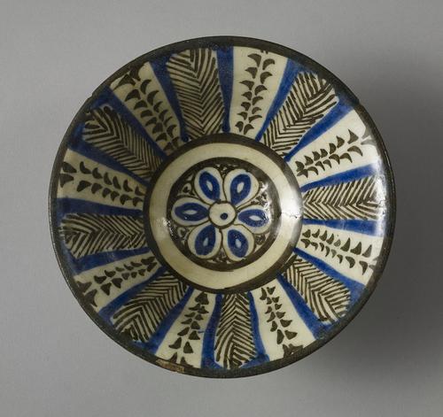 A blue, black and white-glazed pottery bowl, of rounded form with flaring rim on short foot, the interior with central rosette flanked by radiating alterning panels.