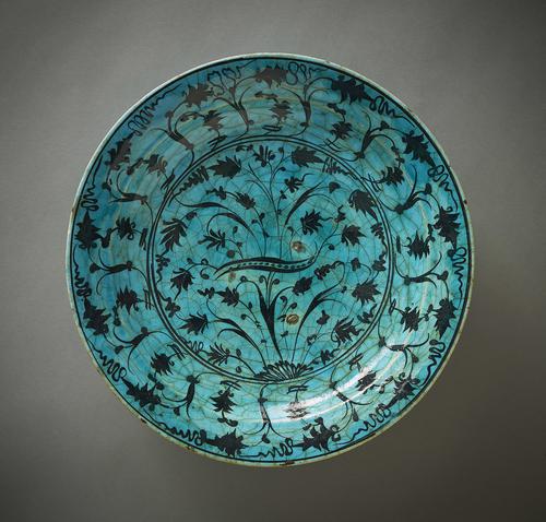 Ceramic dish, with slightly curved body and flat rim, the interior decorated with a series of fowers and stems painted in black against a turquoise-blue ground.
