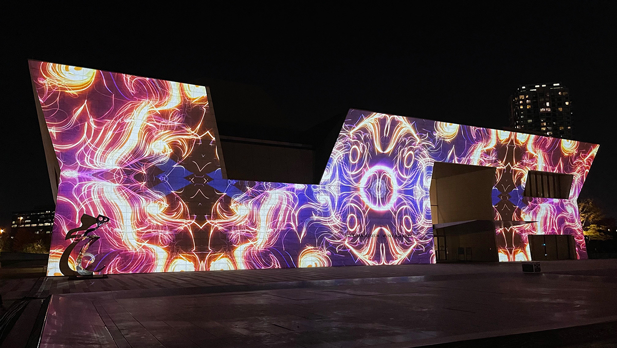 The west facade of the Aga Khan Museum lit up at night with colourful projected patterns.