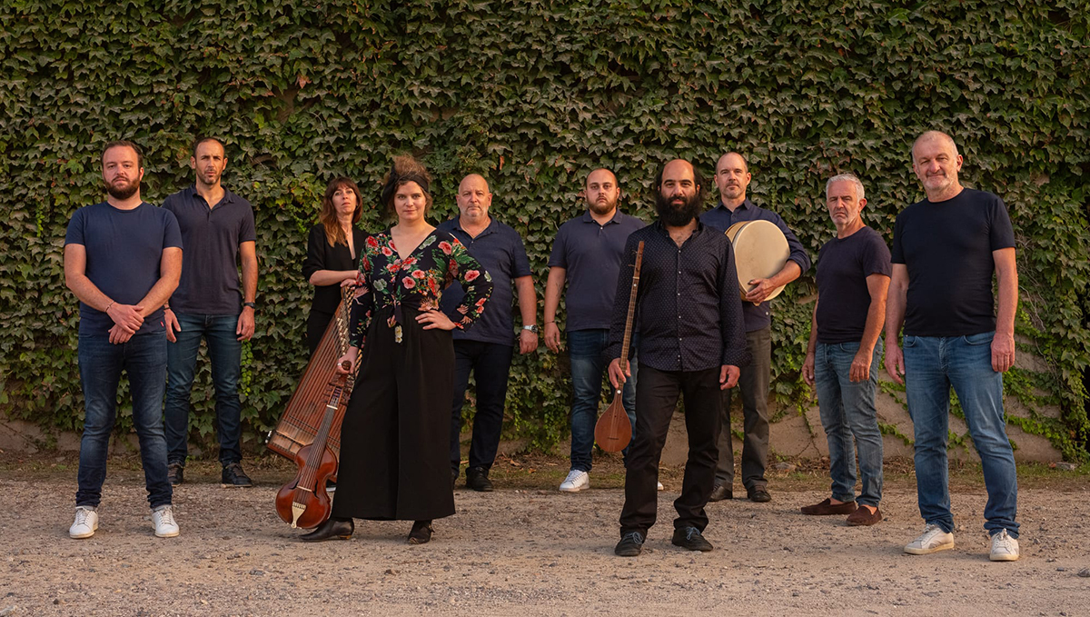 About a dozen musicians pose standing up in front of wall of ivy.