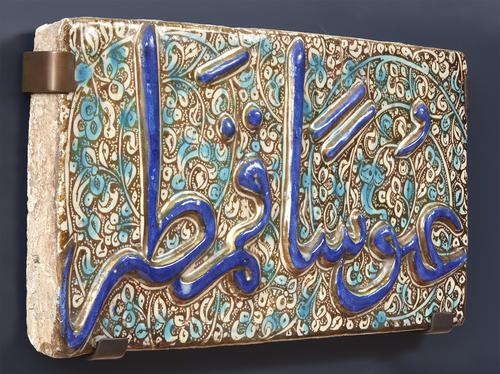 Side of rectangular ceramic tile decorated with arabic calligraphy, mounted on wall.