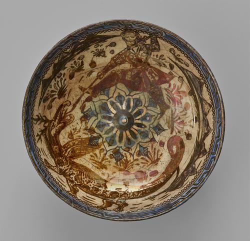 Interior of a bowl with an eight-petalled flower in the center. Around it a semi-arid landscape supports scattered flowers with distant mountains rising near the rim. The landscape is dominated by the figure of a hero, stabbing a huge dragon with a spear