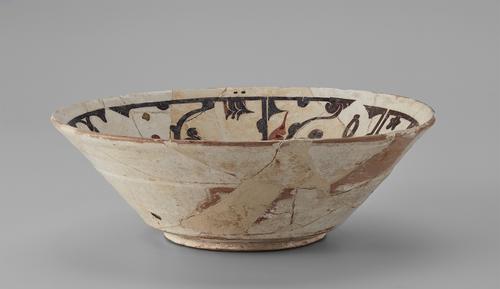 Side of a bowl, with white slip over the reddish body is decorated with a dark brown and red inscription on the sides. Exterior sides show cracking and restoration.