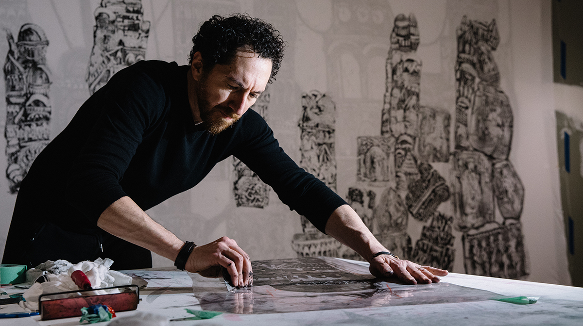 Kevork Mourad creates a work of art at a table in a dark studio.