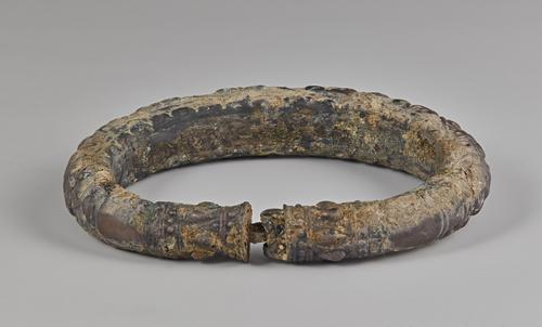 One of two silver arm bracelets, engraved, the back of the bracelet shows the clasp or connection and inside of the bracelet. Showing signs of corrosion on all sides.