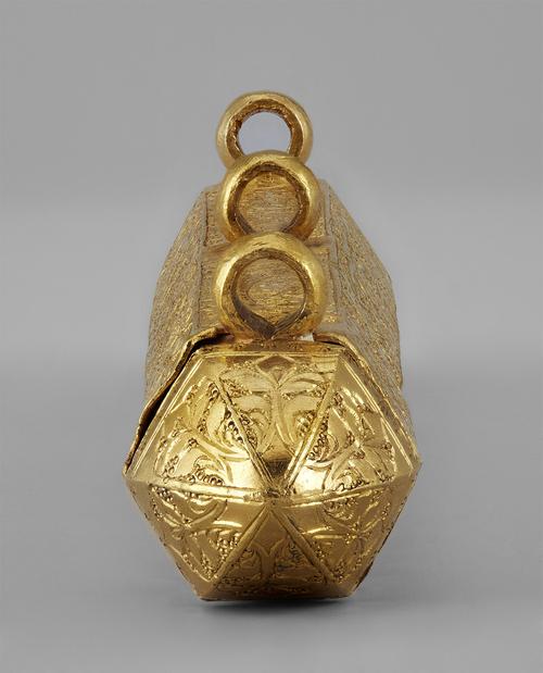 End view of the gold amulet in the shape of a hexagonal prism with pointed ends, looking down the top through the three suspension loops. It is inscribed with Qur’anic verses.
