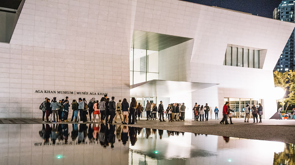 A crowd stands outside the Museum near the reflecting pool at night.