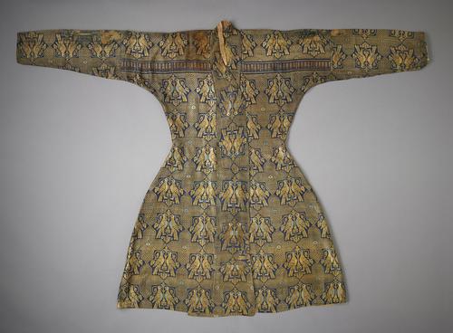 Silk robe, closed and laid flat with the arms extended to the side. The robe is woven with a repeating gold-and-blue pattern of two birds facing each other inside of a geometric star. There is a horizontal band of a contrasting pattern extending from shoulder to shoulder.   