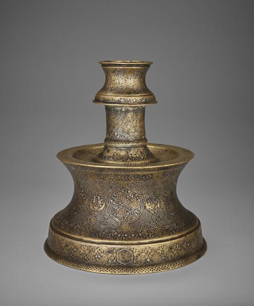 With its truncated engraved body, this candlesticks design consists of interlacing medallions filled with arabesque-like patterns, smaller fretwork medallions, and simple pairs of birds that develop out of the stems and are almost hidden within the foliate scrolls.