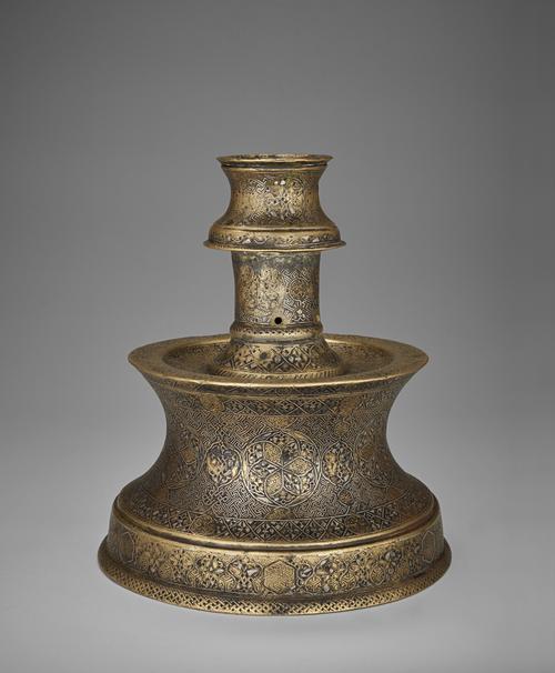 Side view of a candlestick with truncated engraved body, its design consists of interlacing medallions filled with arabesque-like patterns, smaller fretwork medallions, and simple pairs of birds that develop out of the stems and are almost hidden within the foliate scrolls.