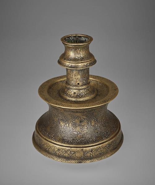 Top view of a candlestick with truncated engraved body, its design consists of interlacing medallions filled with arabesque-like patterns, smaller fretwork medallions, and simple pairs of birds that develop out of the stems and are almost hidden within the foliate scrolls.