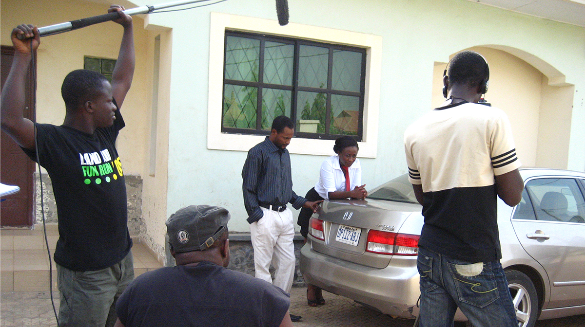 A film crew shoots a scene featuring two actors in the driveway of a house beside a Honda Accord.