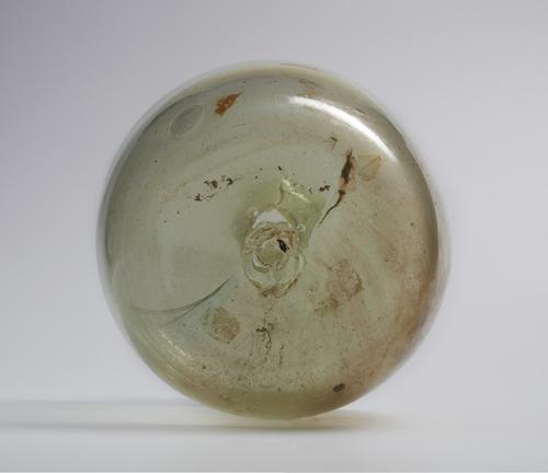 Rounded bottom of short glass bubble shaped bottle blown from colourless glass with a greenish tinge. Visible pontil mark in the middle of the base.