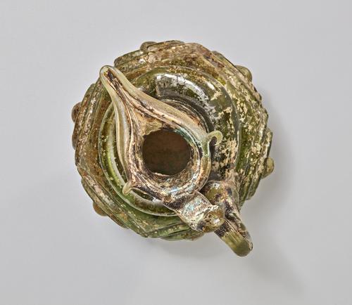 Top down view through the cylindrical neck, of a Green, brown and slightly iridescent glass ewer with an almond-shaped mouth-top