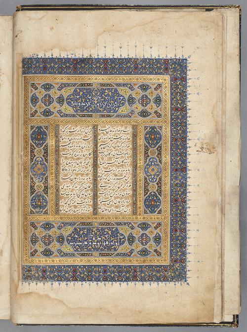 Folio with four verses in black calligraphy, surrounded by gold decoration. The verses are bordered by a large frame, with panels of blue, gold, and red filigree decoration. The top, left, and bottom have blue border panels with trailing decorations that extend to the margins.
